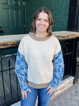 Woman wearing a beige sweater with blue sleeves standing in front of a green door.